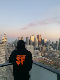 Close-up of a black hoodie with NYC orange and blue bold typography on a gritty urban backdrop.