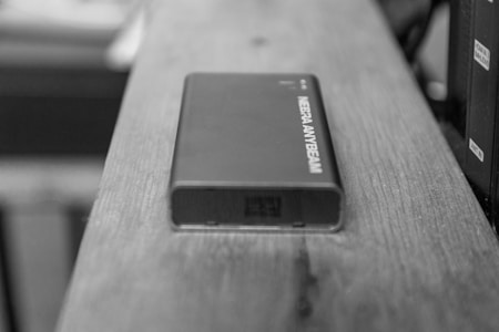 A compact electronic device with the label MEERA ANYBEAM resting on a wooden surface. The device appears to be sleek and rectangular, with a clean, modern design.