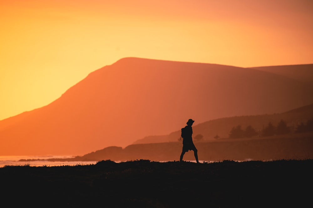 silhouette d’homme debout sur la colline pendant le coucher du soleil