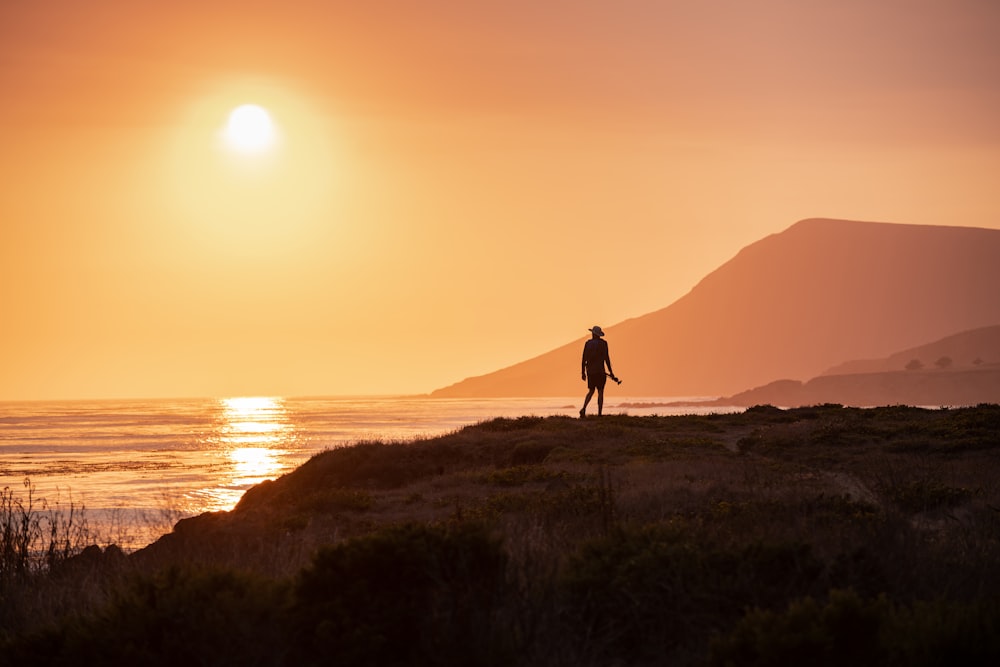 silhouette of person walking on seashore during sunset