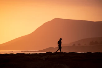 silhouette of man standing on hill during sunset