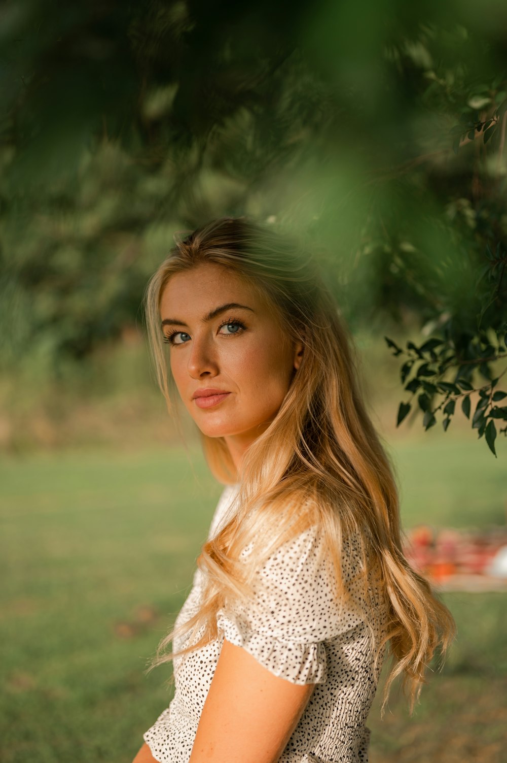 woman in white and brown floral shirt standing near green leaf tree during daytime