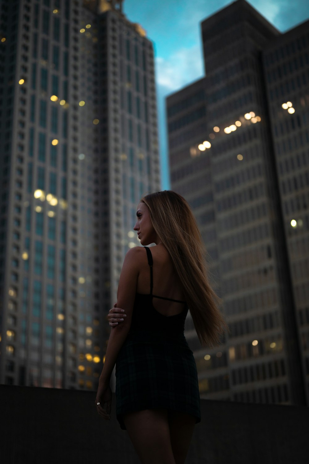 검은 스파게티 스트랩 탑을 입은 여자가 밤 시간에 고층 건물 앞에 서 있다