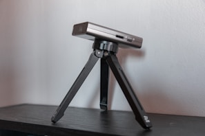 A compact smart mini video projector next to a laptop and coffee cup on a desk.