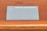 A device labeled Nebra Anybeam is placed on a wooden surface. The device is rectangular and metallic, with two ports labeled HDMI on one end. The surface it rests on is a warm-toned wood with horizontal lines.