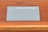 A device labeled Nebra Anybeam is placed on a wooden surface. The device is rectangular and metallic, with two ports labeled HDMI on one end. The surface it rests on is a warm-toned wood with horizontal lines.