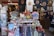 A vibrant storefront displaying a variety of traditional Japanese items including Maneki-neko statues, decorative fans, t-shirts with Japanese motifs, and an assortment of small souvenirs. The arrangement of the items creates an inviting and colorful atmosphere.