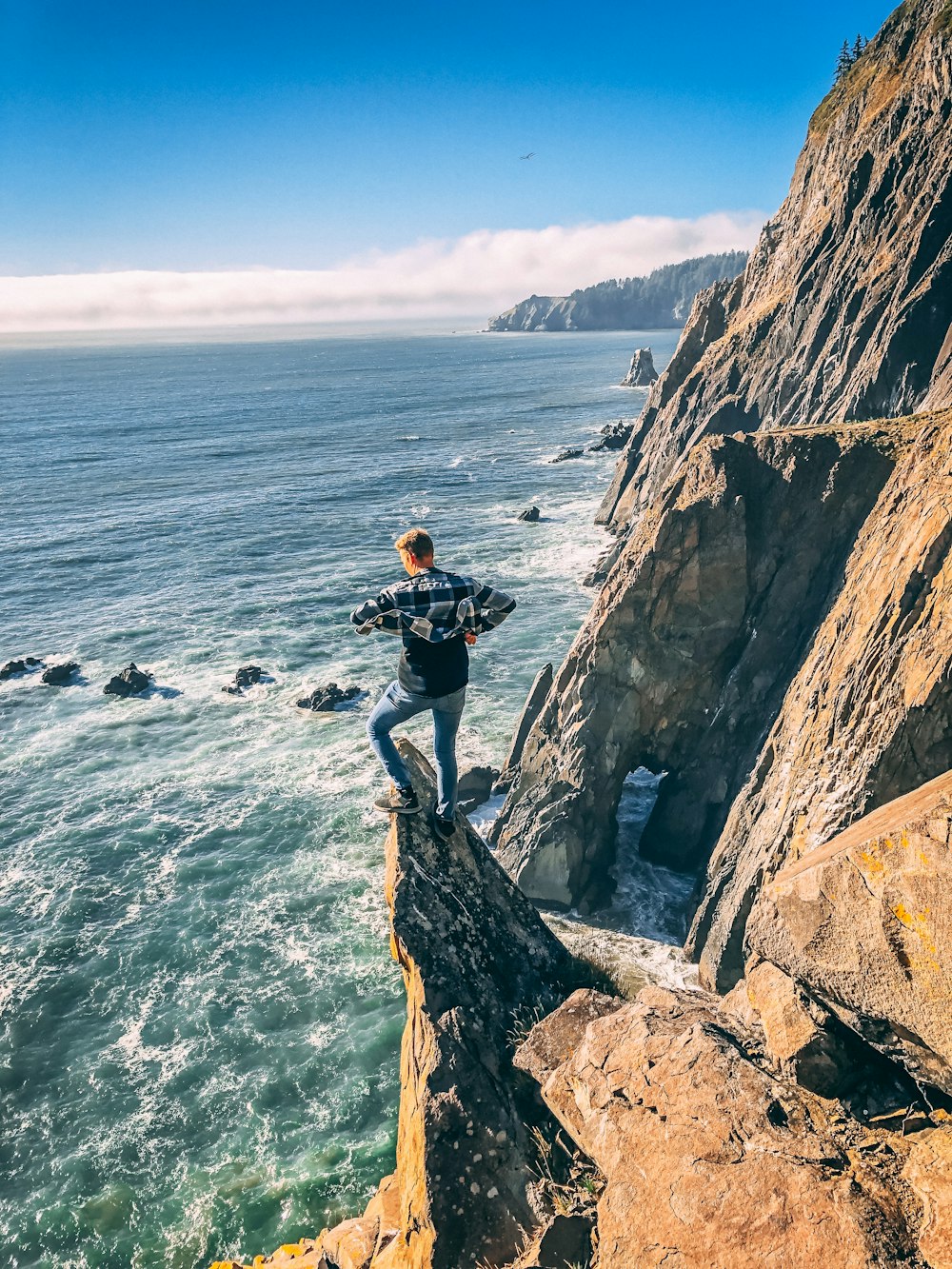 man in black jacket standing on rock formation near body of water during daytime