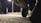A close-up view of the tire of a vehicle, positioned in the foreground against a blurred background featuring a street lamp and pavement. The scene is captured at night, creating a moody, dimly-lit atmosphere with the focus on the shiny detail of the tire.