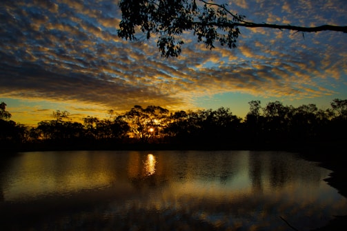 Sunset over a tranquil lake reflecting the deep colors of the sky and surrounding trees.