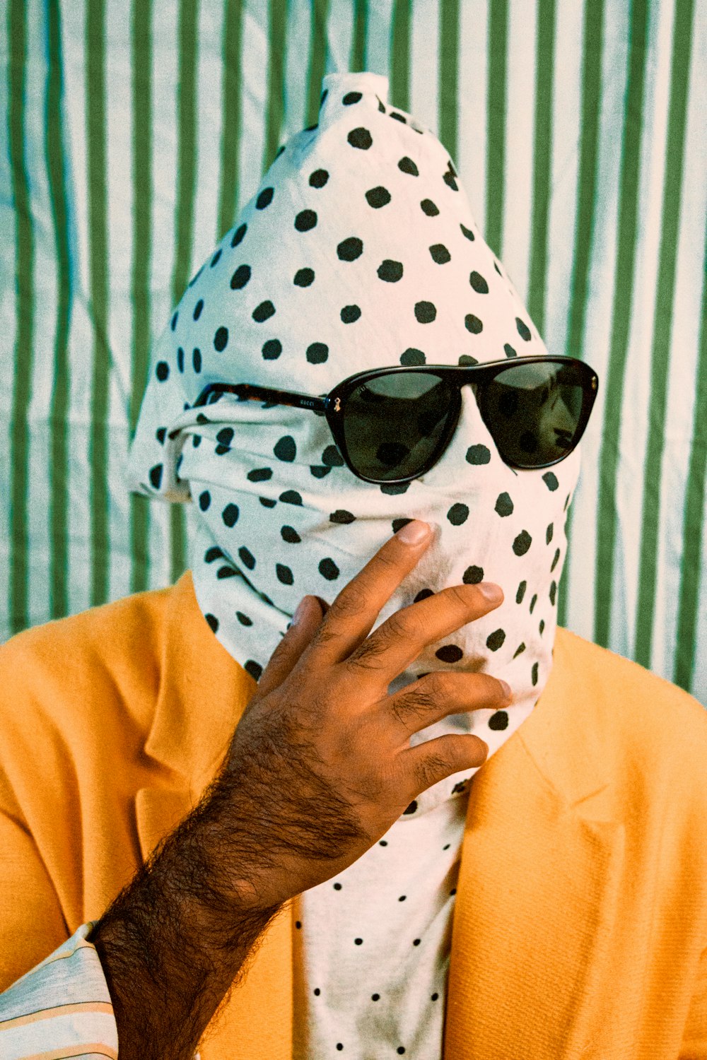 Person im gelben Langarmhemd mit schwarz-weißem Polka-Dot-Schal und schwarzer Sonnenbrille