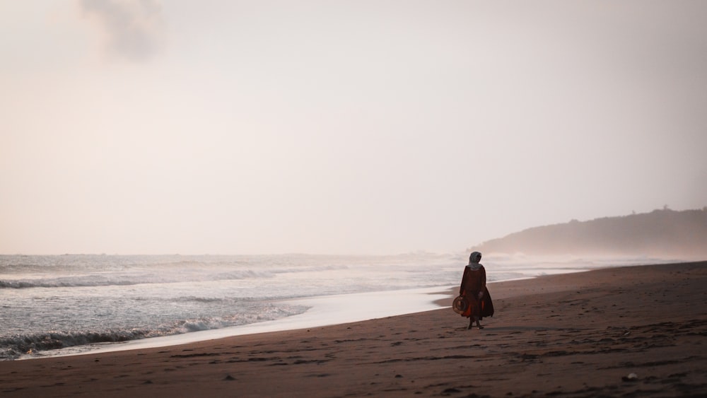 woman in black jacket walking on beach during daytime