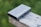 A portable external hard drive is placed on a wooden surface with a blurred green background. The device is rectangular with rounded edges and features ports on the side.