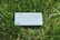 A device labeled 'NEBRA ANYBEAM' is placed on a bed of green grass. The device is rectangular and appears metallic or plastic, with two small round indicators on the top.