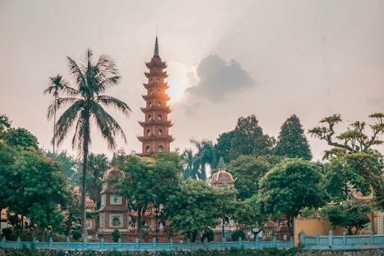 brown and white concrete building near green trees under white clouds during daytime in Tran Quoc Temple Vietnam