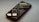 A smartphone lies on its back on a smooth surface, displaying lines of code and programming text on its screen. The screen brightness creates a soft glow, and the reflection shows the text in reverse. The phone is angled slightly to the side, partially out of focus.