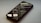 A smartphone lies on its back on a smooth surface, displaying lines of code and programming text on its screen. The screen brightness creates a soft glow, and the reflection shows the text in reverse. The phone is angled slightly to the side, partially out of focus.