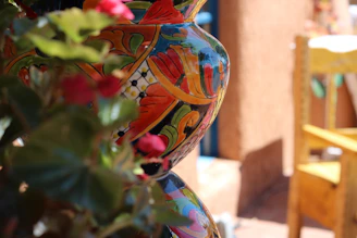 Close-up of a hand-painted ceramic vase with bright floral patterns, sitting beside a cozy window nook.