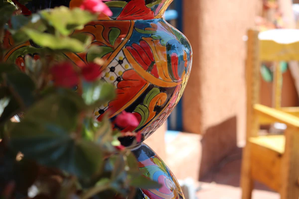Close-up of a hand-painted ceramic vase with bright floral patterns, sitting beside a cozy window nook.