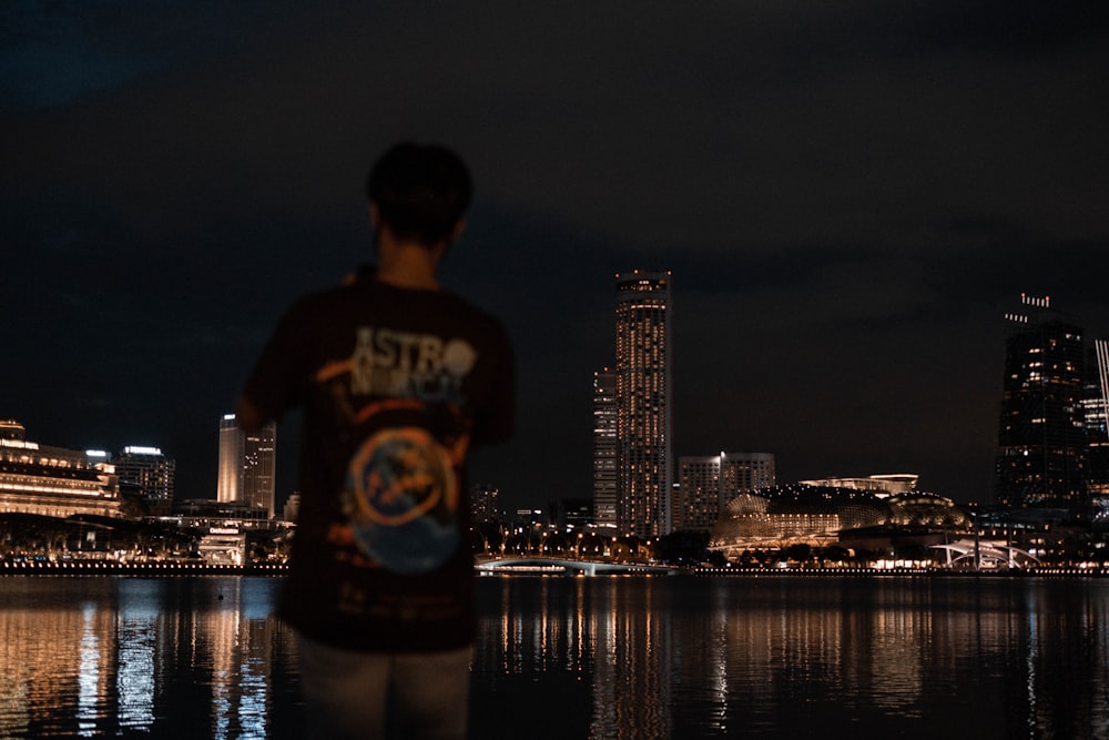 man in white and black crew neck t-shirt standing near body of water during night