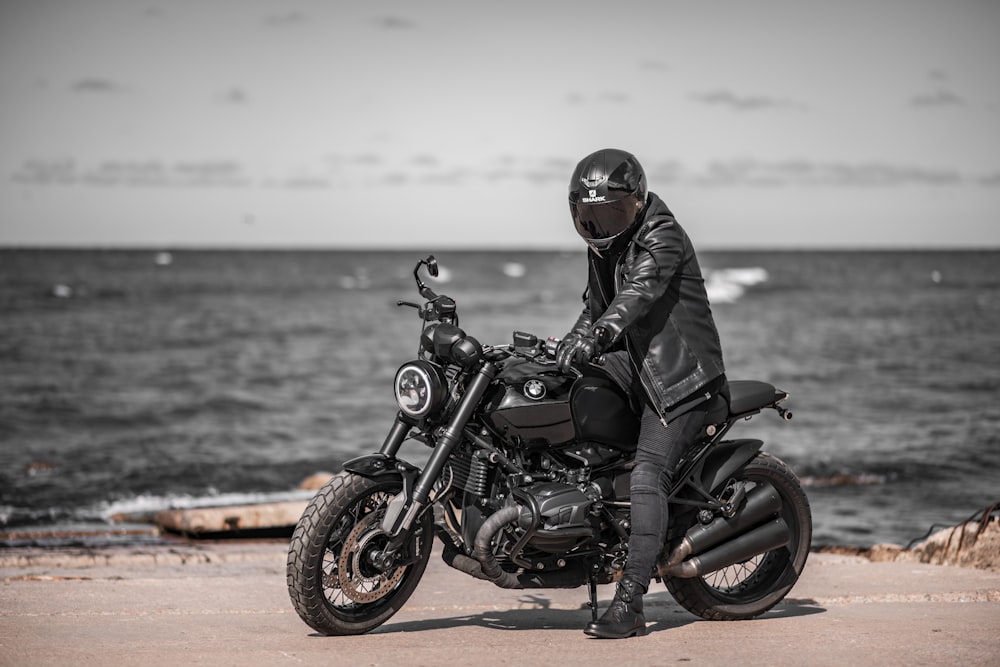 man in black leather jacket riding black motorcycle on brown sand during daytime