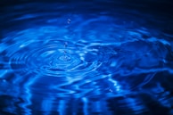 Ripples on a vibrant blue water surface with a droplet captured in mid-air, creating concentric circles.
