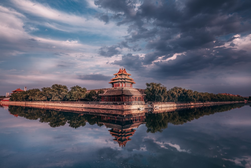 brown and green temple near body of water under cloudy sky during daytime