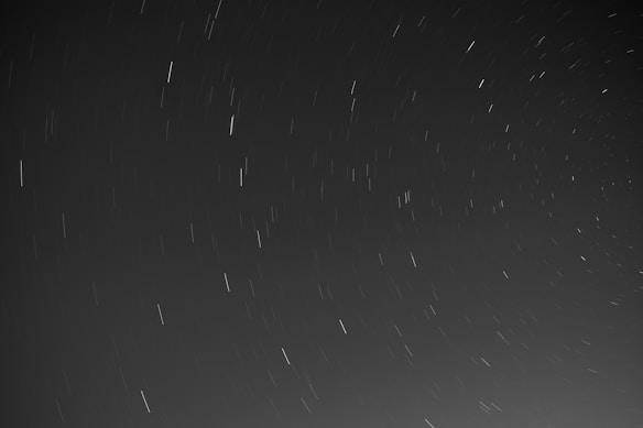 Long exposure photograph capturing star trails across a dark night sky, creating streaks of light as the stars appear to move due to Earth's rotation.