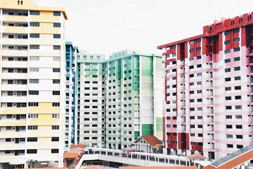 High-rise residential buildings painted in diverse colors including yellow, green, and red. The structures feature numerous windows and balconies, with uniform design and spacing. Roofs of smaller structures with reddish tiles are visible in the foreground.
