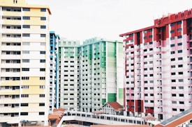 High-rise residential buildings painted in diverse colors including yellow, green, and red. The structures feature numerous windows and balconies, with uniform design and spacing. Roofs of smaller structures with reddish tiles are visible in the foreground.