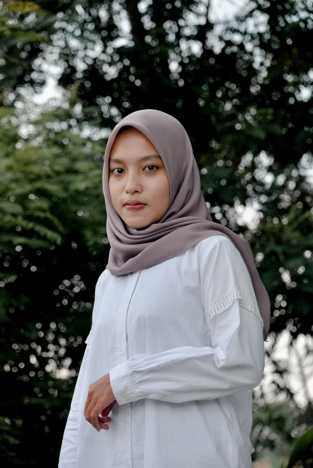 woman in white hijab standing near green trees during daytime