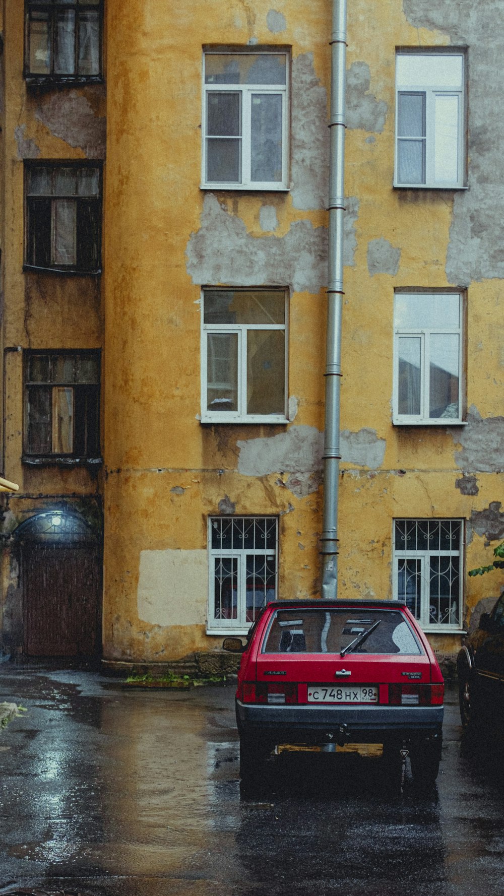 red car parked beside brown concrete building during daytime