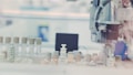 A laboratory setting with a robotic arm interacting with test tubes that have various colored caps, arranged on a tray. The background has a blurred effect, creating a focus on the equipment.