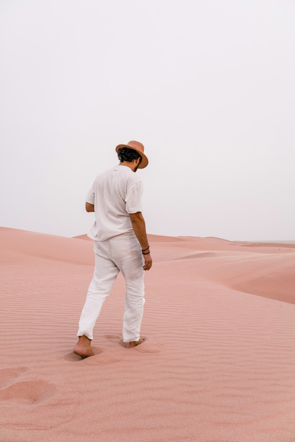 man in white long sleeve shirt and white pants walking on desert during daytime