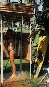 woman in black bikini bottom and yellow shorts standing near green banana tree during daytime