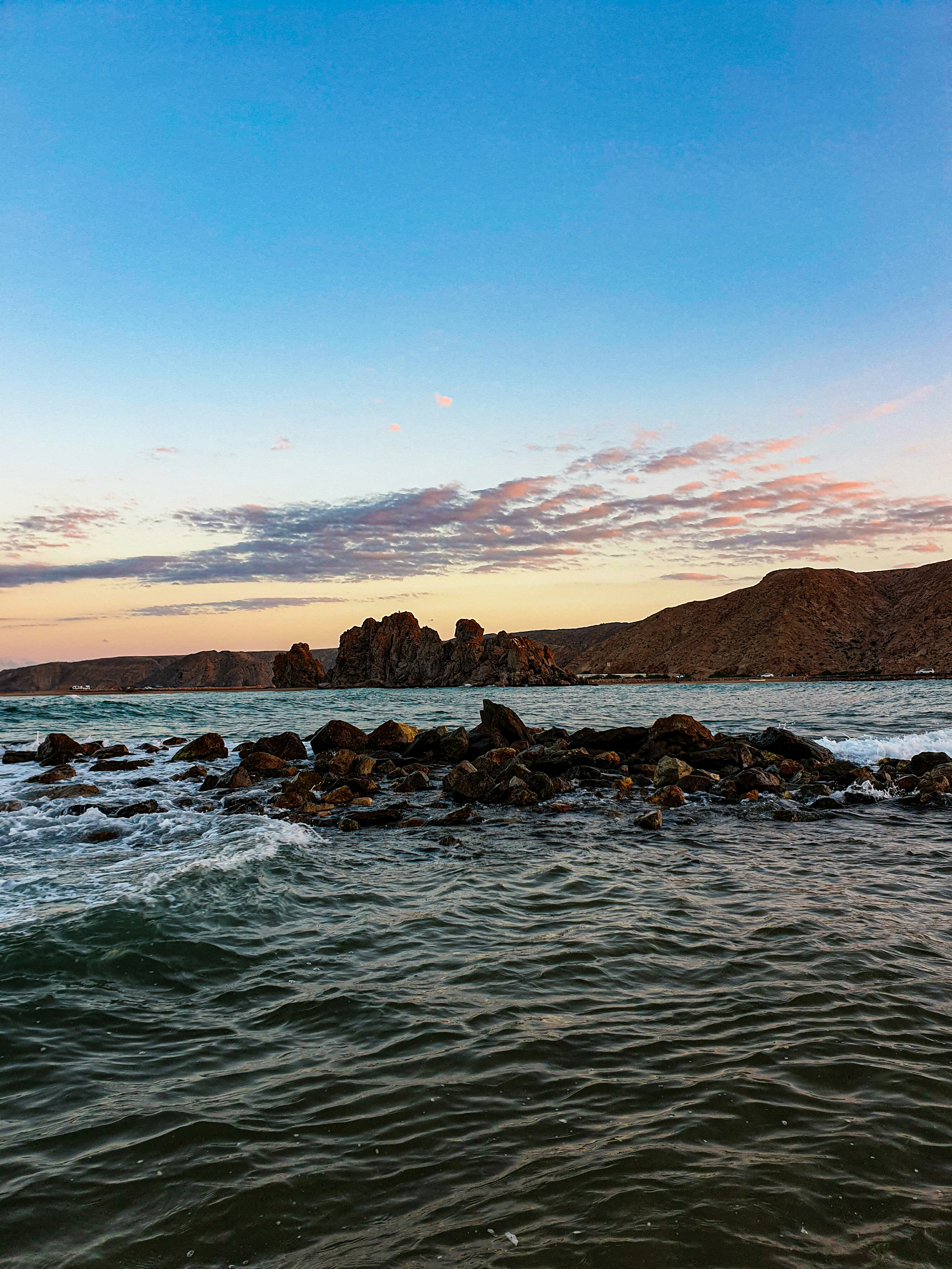 costa rochosa com rochas e montanha à distância sob o céu azul durante o dia