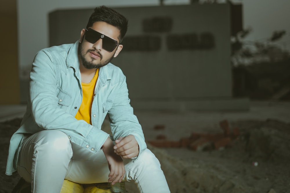 man in blue dress shirt and white pants wearing black sunglasses sitting on brown wooden bench