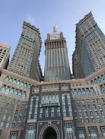 A large and intricately designed building with a prominent clock tower at the center, flanked by two symmetrical wings. The architecture features a mix of modern and traditional elements, with numerous windows and decorative arches.