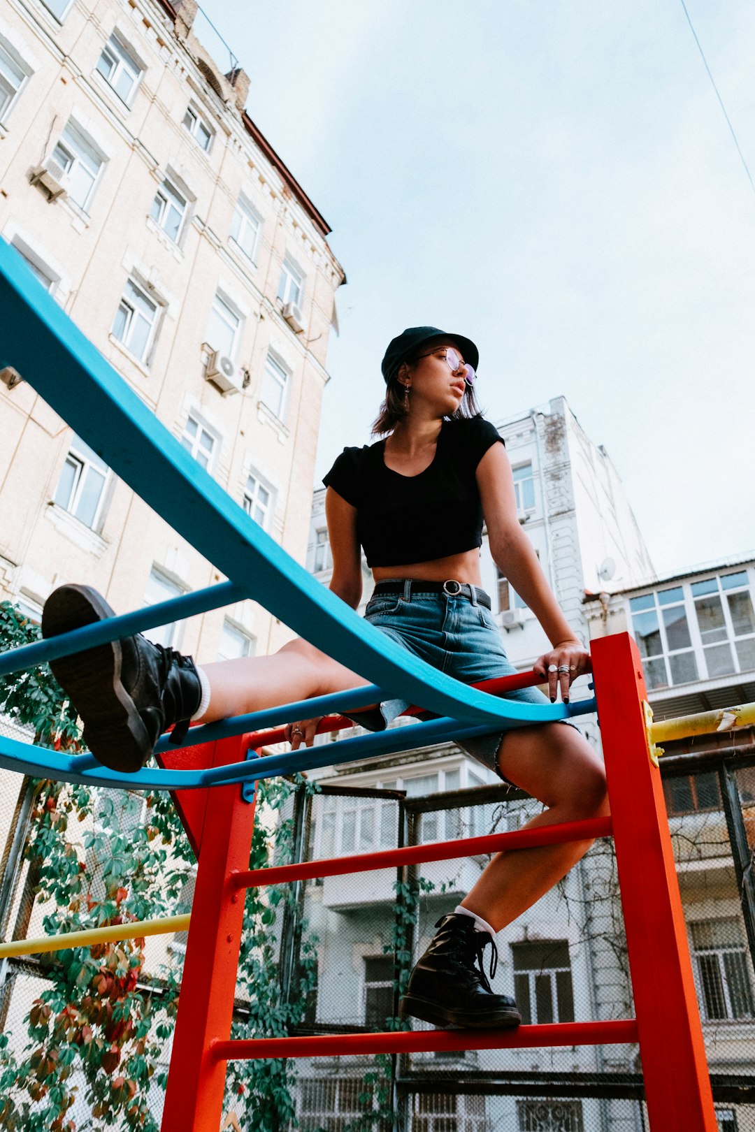 woman in black tank top and blue denim shorts sitting on blue metal railings during daytime