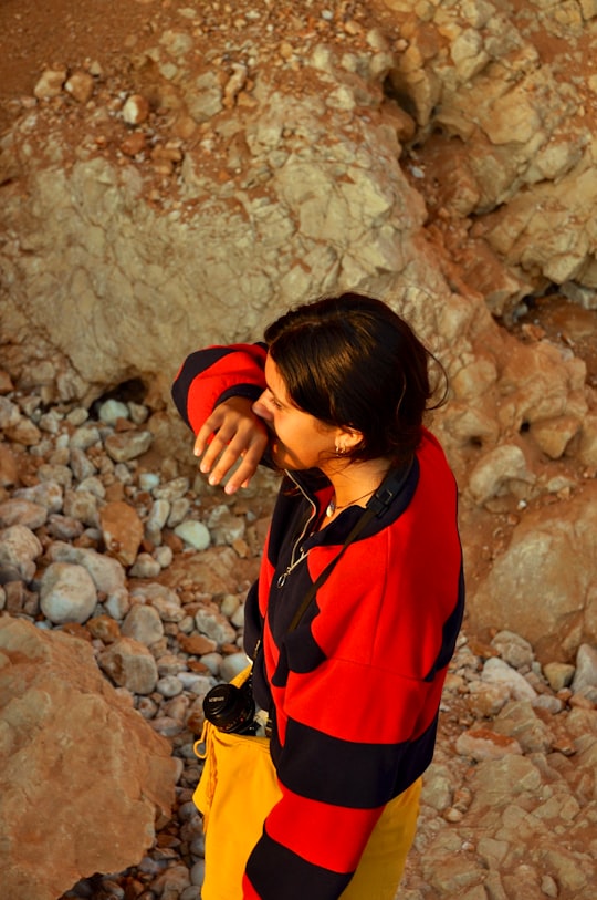woman in red and black jacket standing near brown rock in Sagres Portugal