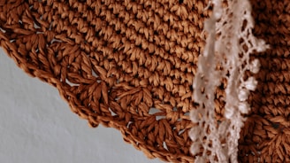 Detailed close-up of a woven mat with a rich, brown color and intricate textures. There is a white, delicate lace fabric placed on top of the mat, partially draped over the edge.