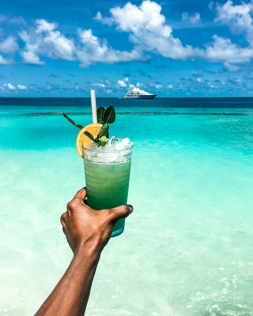 person holding clear drinking glass with green liquid and straw