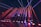 Bright colored laser beams in red and blue cut across a darkened room, originating from a stage with a DJ booth that displays a logo. The beams reflect off the glossy floor, creating a dynamic and energetic atmosphere.