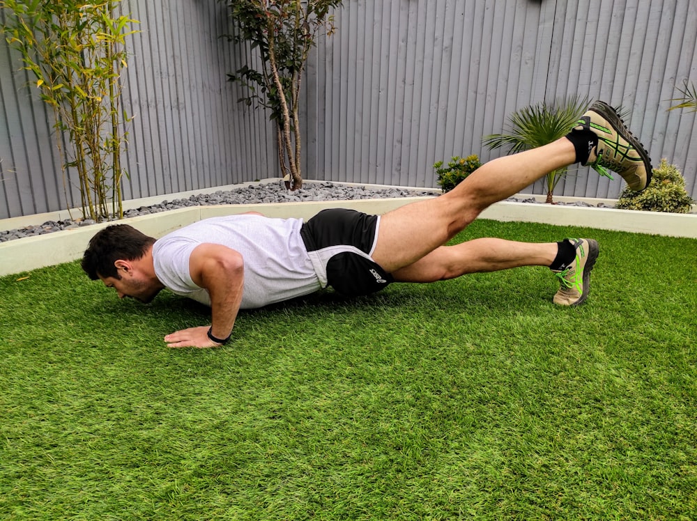 man in white tank top and black shorts lying on green grass field during daytime