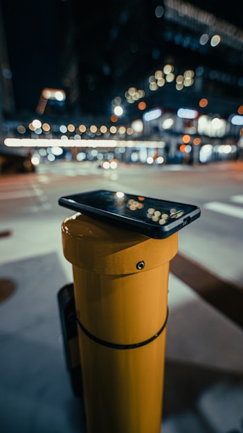 A sleek, modern smartphone resting on a city bench with blurred urban lights in the background.
