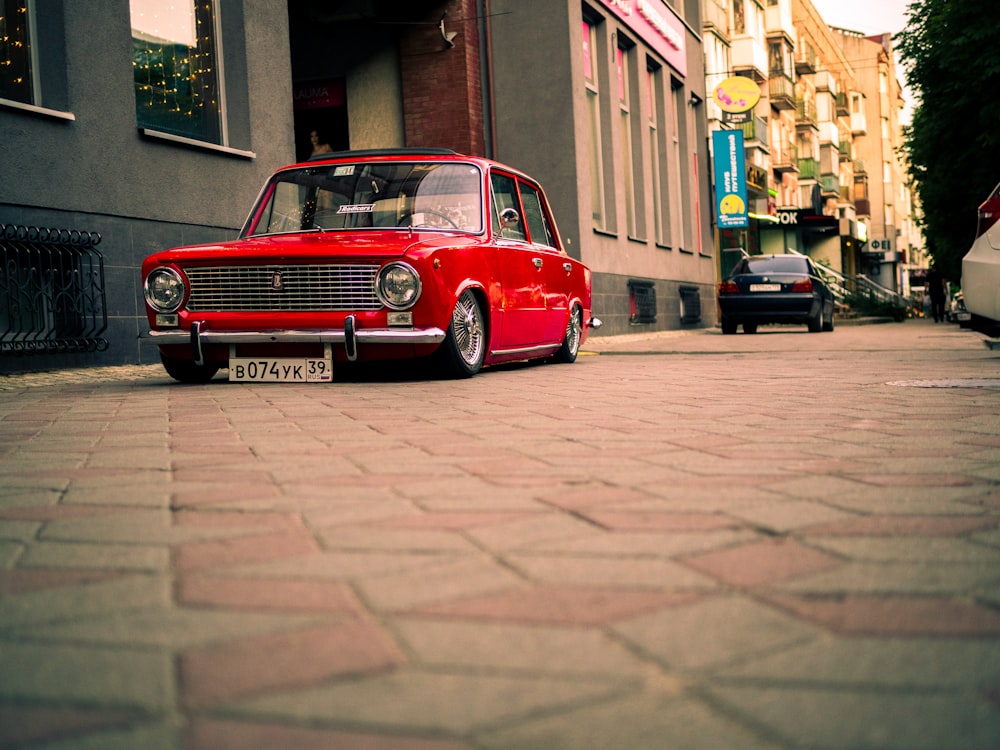 red car parked beside brown brick building during daytime