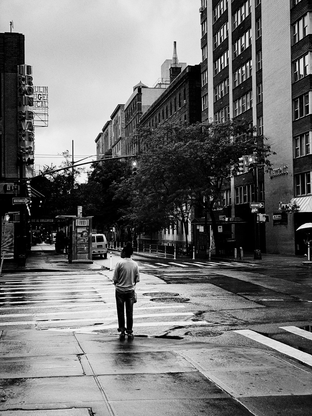 man in white shirt walking on street in grayscale photography