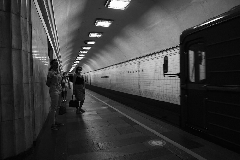 grayscale photo of man in black jacket standing beside train