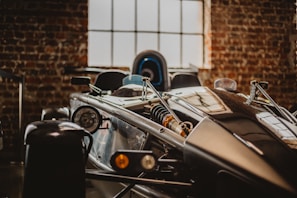 A close-up view of a sleek, modern race car with visible mechanical components such as the suspension and headlight, set against a background of exposed brick walls and a large window.
