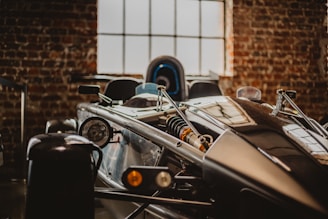 A close-up view of a sleek, modern race car with visible mechanical components such as the suspension and headlight, set against a background of exposed brick walls and a large window.